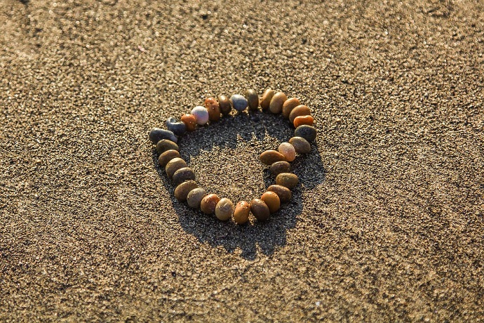 A heart made of small stones on the sand at the beach.